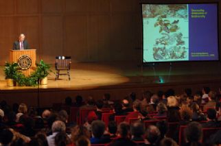 EO Wilson speaking to the crowd with a slide presentation in the background