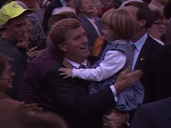 Dan Quayle carrying a child through a crowd